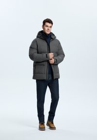 Gray padded jacket with a hood, featuring a zip front and black accents. Paired with dark jeans and brown lace-up boots.