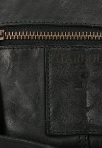 Schwarze Lederinnentasche mit einem bronzenen Reißverschluss und einem geprägten Patch mit Ankerdesign und dem Text "HARBOUR 2nd." Glatte Textur, minimale Details.