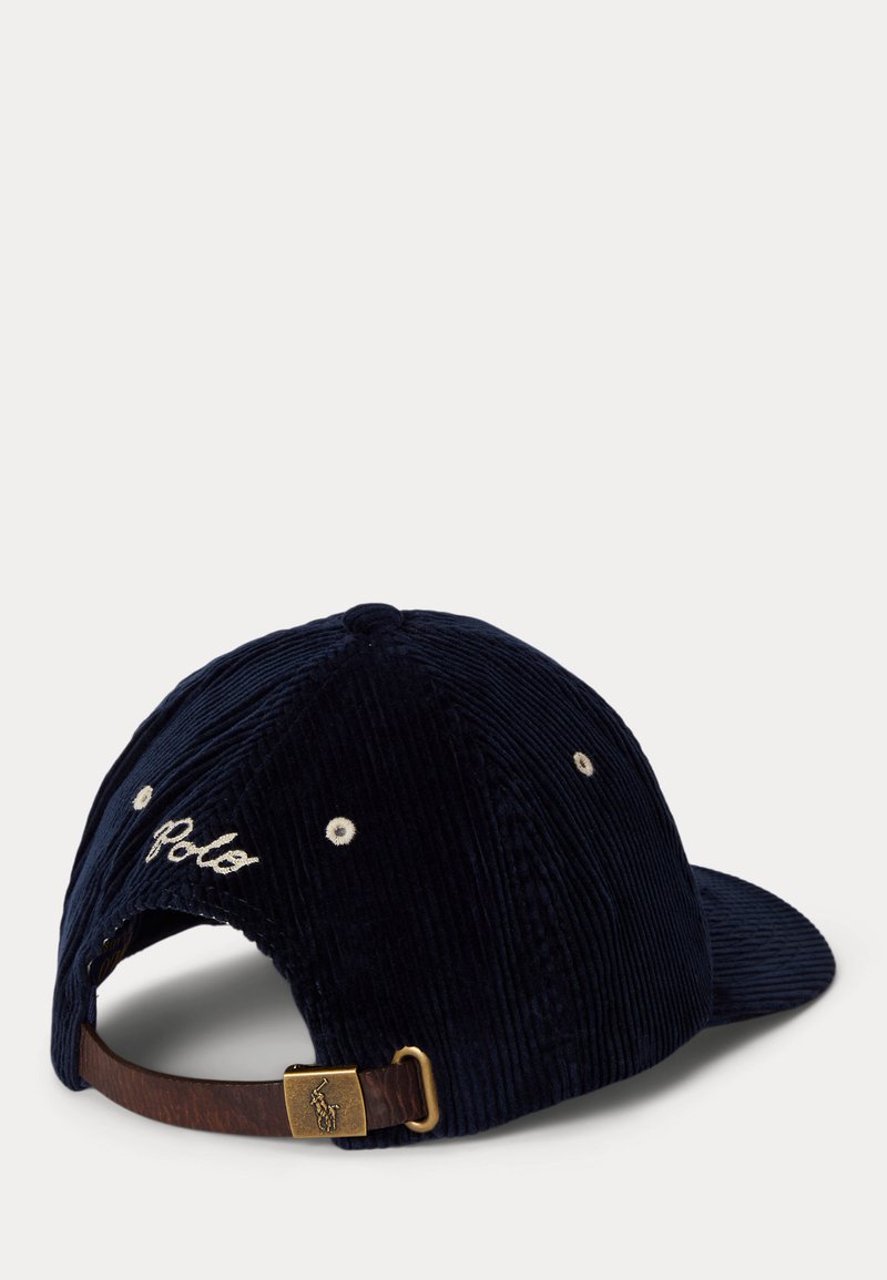Marineblaue Cordmütze mit verstellbarem braunem Lederband und messingfarbenen Beschlägen, mit "Polo" in Weiß auf der Rückseite gestickt.