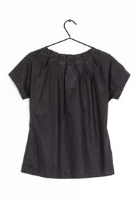 Haut noir à manches courtes avec un col rond, tissu doux, détails plissés sur le devant et ourlet arrondi. Suspendu à un crochet noir.