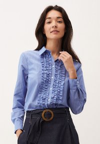 Blauw-wit gestreepte blouse met een ruffle detail aan de voorkant, een button-down kraag, lange mouwen en manchetten met knoopsluitingen.