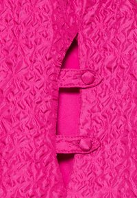 Fuchsia strukturerad tyg med ett upphöjt mönster. Har två matchande knappar på en klaff som avslöjar en slät insida i samma färg.