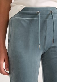 Svetle modré tepláky vyrobené z měkké texturované látky, s elastickým pasem s tkaničkou a bočními kapsami.