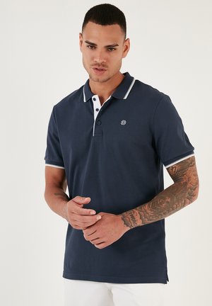 Mornarsko polo majica s bijelim ovratnikom i manžetama, kratkim rukavima, izvezenim logotipom na prsima i klasičnim krojem s bočnim prorezima na rubu.