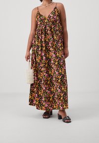 Maxiklänning med blommönster i rosa, orange och gult på svart bakgrund; har tunna axelband och en lös, flödande design.