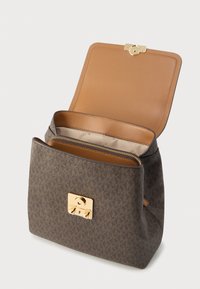 Ruskea kuvioitu käsilaukku, jossa on kullanvärinen metallilukko. Sisäpuolella beige vuori, jossa vetoketjutasku ja sileä pinta.