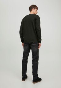 Zwarte trui met lange mouwen, geribbelde manchetten en een V-hals, gecombineerd met donkere spijkerbroek en zwarte sneakers. Soepele textuur, minimale details.