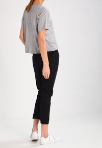 Graues kurzärmliges, cropped T-Shirt, schwarze enganliegende Hose und weiße Sneaker, die ein lässiges, bequemes Outfit aus seitlicher Sicht zeigen.