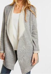 Grå cardigan med en kviltad textur och en kontrasterande ljus insida. Öppen framsida med långa ärmar och en avslappnad passform.