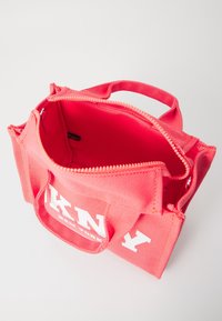 Różowa torba na zakupy z mocnymi uchwytami, zamknięciem na zamek błyskawiczny i białym logo. Wnętrze jest wyłożone, z prostym, użytkowym wzornictwem.