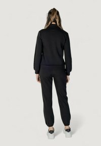 Set atletico nero composto da una giacca con zip e polsini elastici e pantaloni jogging abbinati con caviglie elastiche. Il materiale sembra morbido e comodo.
