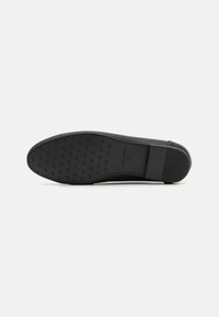 Semelle de chaussure habillée noire, présentant un motif de grip texturé, un bord lisse et un logo en relief. Design épuré avec un bout arrondi et des accents minimalistes.
