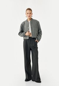 Grå cropped bomberjakke med rund halsudskæring, frontknapper og ribbede ærmer, parret med højtaljede mørke bukser.