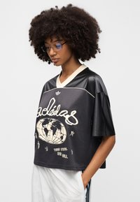 Mustast lühendatud jerseyst koos võrgutekstuuriga, millel on valge maakera graafika ja tekst. Koorivärvi soonikkoes krae ja lühikesed varrukad.