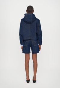 Denim hættebluse med cropped pasform og hætte, parret med matchende denimshorts. Mørkeblå farve, synlige stikninger og et afslappet design.