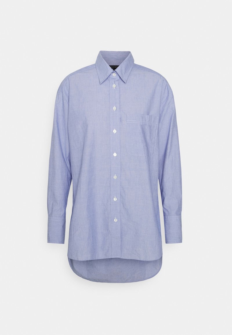 Light blue button-up shirt made of textured cotton, featuring long sleeves and a chest pocket, with a curved hem at the bottom.