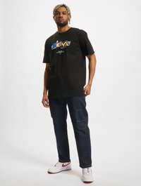 Black graphic t-shirt featuring "BKLYN" in colorful text. Paired with dark denim pants and white sneakers with red accents.