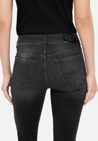 Jeans de mezclilla negra con un diseño ajustado, que presentan una textura suave, dos bolsillos traseros y costuras decorativas en los bolsillos.