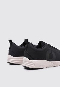 Zapatillas deportivas negras con un upper de textil suave, que presentan un acento de logo y una suela de goma blanca contrastante. Diseño minimalista con tirador.