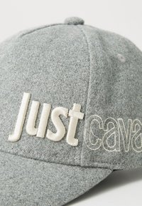 Sivá teksturirana bejzbol kapa z dvignjenim vezenjem z napisom "Just cava" v kremni niti čez sprednjo ploščo in rob.