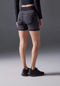 Mustat urheilushortsit, joissa on verkkopaneeli ja abstrakti harmaa kuvio. Shortsissa on leveä vyötärönauha ja istuva malli, yhdistettynä mustiin lenkkareihin.