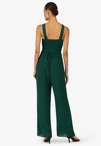 Donkergroene, wijde jumpsuit met een gerimpelde lijfje en brede bandjes. Lichte stof creëert een vloeiende silhouet.