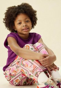 Chemise violette à manches courtes, pantalon coloré avec des motifs floraux et géométriques, et baskets blanches avec des accents pastel.