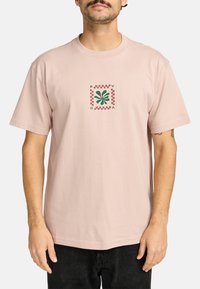 Lichtroze katoenen t-shirt met korte mouwen, voorzien van een groene grafische afbeelding in een vierkant met rode geruite accenten aan de voorkant.