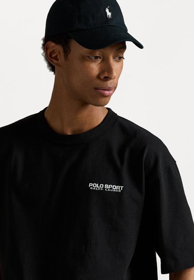 Zwarte katoenen T-shirt met het logo "POLO SPORT RALPH LAUREN" in het wit, gedragen met een zwarte pet met een witte geborduurd logo.
