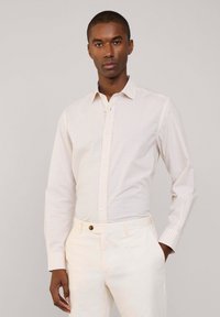 Camisa con botones de cuadros en colores claros, presenta mangas largas, cuello y tapeta delantera. Se lleva con pantalones de color claro.