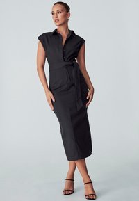 Vestido midi negro de botones con mangas cortas, cintura ajustada y cinturón anudado. Tela suave con una silueta estructurada. Abertura lateral.