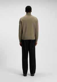 Light olive green knit sweater with a high collar, fitted hem, and long sleeves, paired with black loose-fitting trousers.