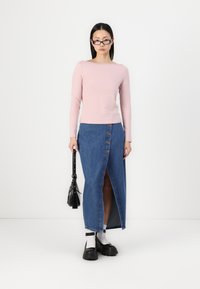 Lys rosa langermet topp, blå denim maxi skjørt med frontspalte og knappdetaljer, svart håndveske og kraftige svarte sko.