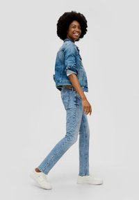 Denimjack en skinny jeans in lichtblauw. Slim fit, iets vervaagd, met voorzakken en contrasterende stiksels. Witte sneakers maken de look compleet.