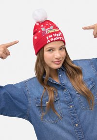 Gorro de punto rojo con pompón blanco y patrones de copos de nieve. El texto dice "NO SOY PAPÁ NOEL." Usado por una persona con una camisa vaquera.
