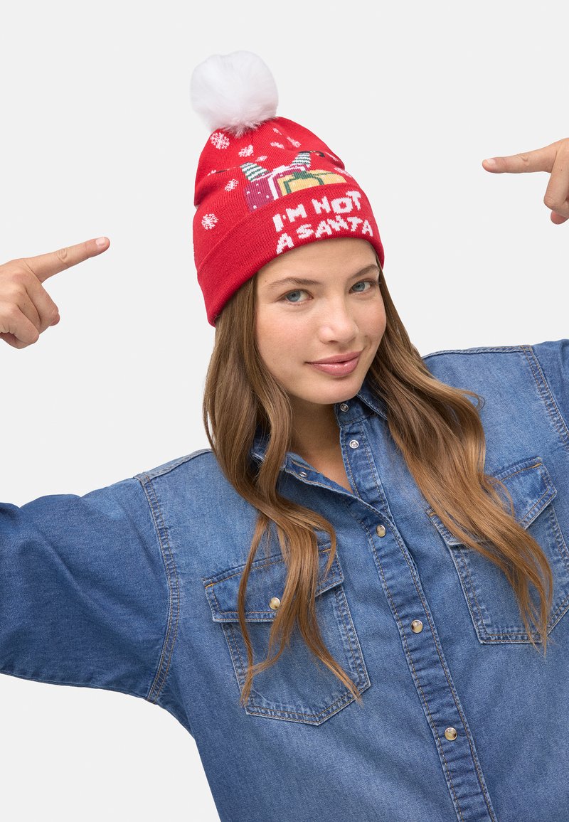 Gorro de punto rojo con pompón blanco y patrones de copos de nieve. El texto dice "NO SOY PAPÁ NOEL." Usado por una persona con una camisa vaquera.
