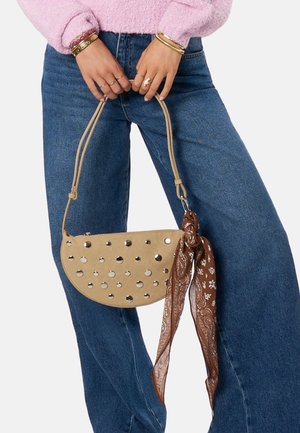 Beige Handtasche mit metallischen Verzierungen, halbmondförmig, glatte Textur und ein braun gemusterter Schal, der an dem Tragegurt gebunden ist.