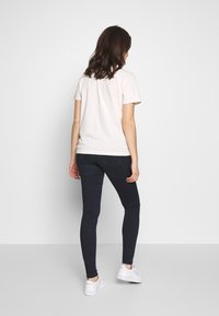 T-shirt de manga curta creme combinado com jeans skinny escuros e ténis brancos. A t-shirt tem um design simples e um corte clássico.
