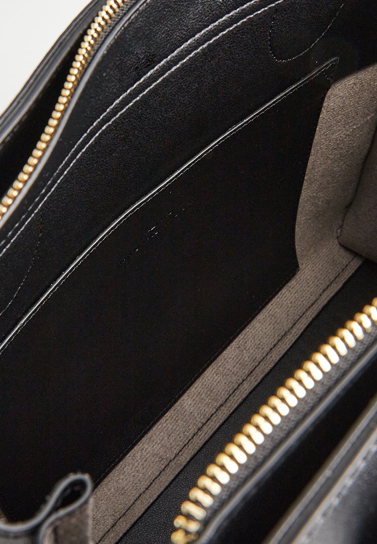 Intérieur en cuir noir d'un sac, avec une texture lisse et une quincaillerie en métal doré. Comprend plusieurs compartiments et une doublure douce.