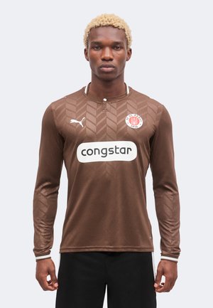 Jeune homme aux cheveux blonds courts portant le maillot de football marron du F.C. St. Pauli avec le logo Puma et le sponsor Congstar.