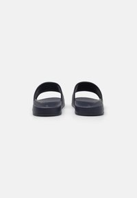 Sandales en caoutchouc noires avec un dos ouvert, dotées d'une semelle plate, d'une texture lisse et d'un design simple ; sans quincaillerie ni accents décoratifs.