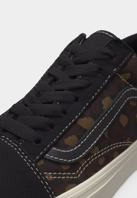 Baskets à imprimé léopard noir et marron avec des lacets noirs, des coutures blanches et une semelle blanc cassé, présentées en gros plan.