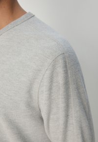 Graues Langarmshirt mit strukturierter Rippoptik, Rundhalsausschnitt und kontrastierenden Nähten an der Schulternaht.