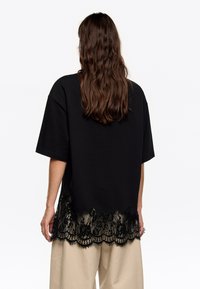 Must mustaga, millel on laineline must pitsäär ja lõdva lõikega, kombineeritud heledate beežide pükstega.