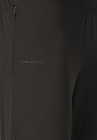 Nahaufnahme von schwarzen Sportshorts mit Reißverschlusstasche und "ENDURANCE" Logo-Detail auf dem Stoff.