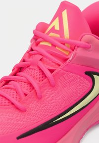 Jasnoróżowy but sportowy z siateczkową cholewką, płaskimi sznurowadłami i czarnym logo w kształcie łyżwy. Posiada teksturowany wzór oraz złoty akcent z logo na pięcie.