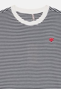 T-shirt rayé noir et blanc avec un col rond, présentant une petite broderie en forme de cœur rouge sur la poitrine. Matière en coton douce.