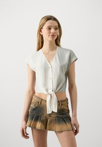 Hvit kortermet bluse med V-hals og frontknyting. Kombinert med en denimskjørt med gradient fra lys til mørk blå og plissert kant.