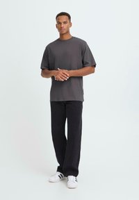 T-shirt in cotone grigio scuro con vestibilità comoda e maniche corte, abbinato a pantaloni neri larghi e sneakers bianche con strisce nere.