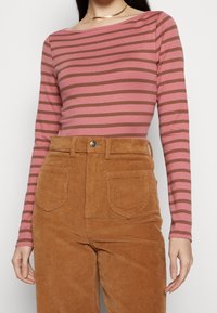Långärmad topp i rosa med bruna horisontella ränder. Matchad med höga corduroybukser i en tan färg, med framfickor.